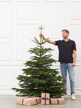 Mand står ved siden af juletræ, for at vise størrelsen på træet.